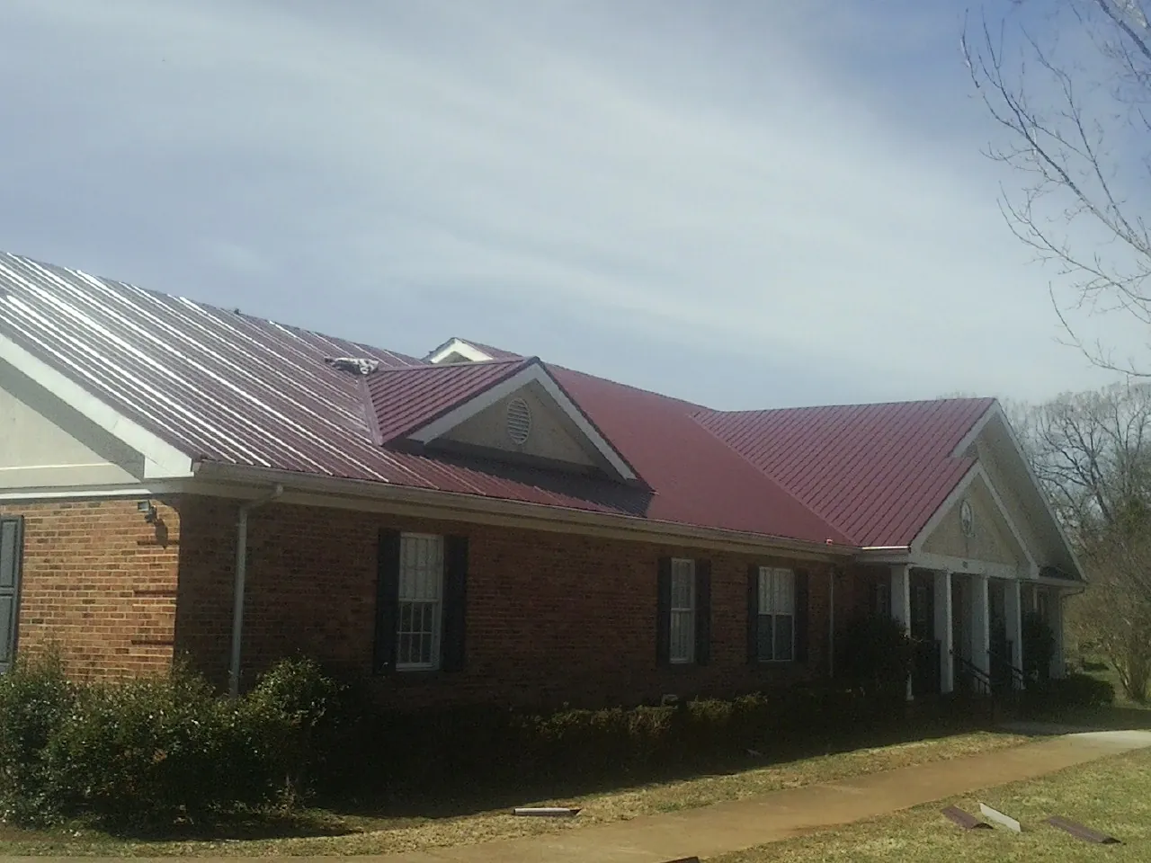 Red metal roof with gabled entries on a long brick building, from a Hail Damage Roof Repair job in Exira