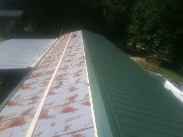 Old rusted panels beside newly installed green metal roofing — Wind Damage Roof Repair by Roofing Brothers in Exira