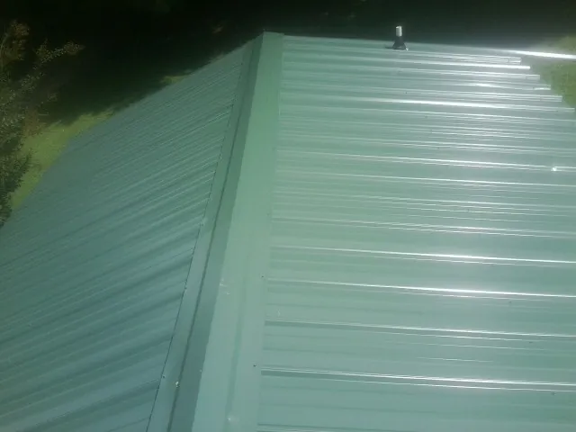 New green metal panels meeting at the ridge of a roof — Flat Roof Repair work by our crew in Exira