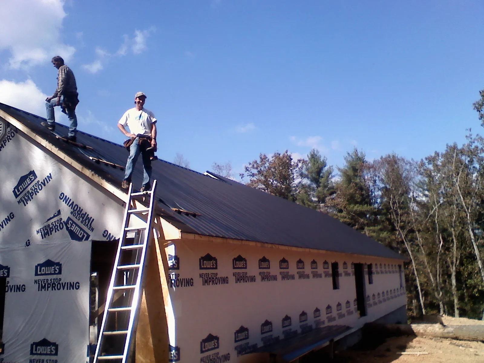 Two roofers standing on a long dark metal roof over a wrapped building in Exira