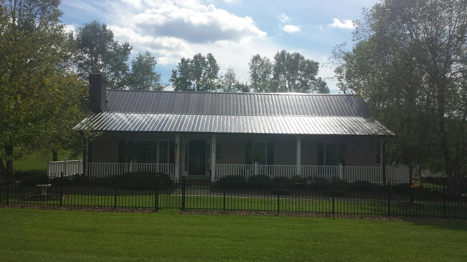 Gray metal roof on a brick ranch with a full width front porch — Gutter Guard Installation work by our crew in Exira