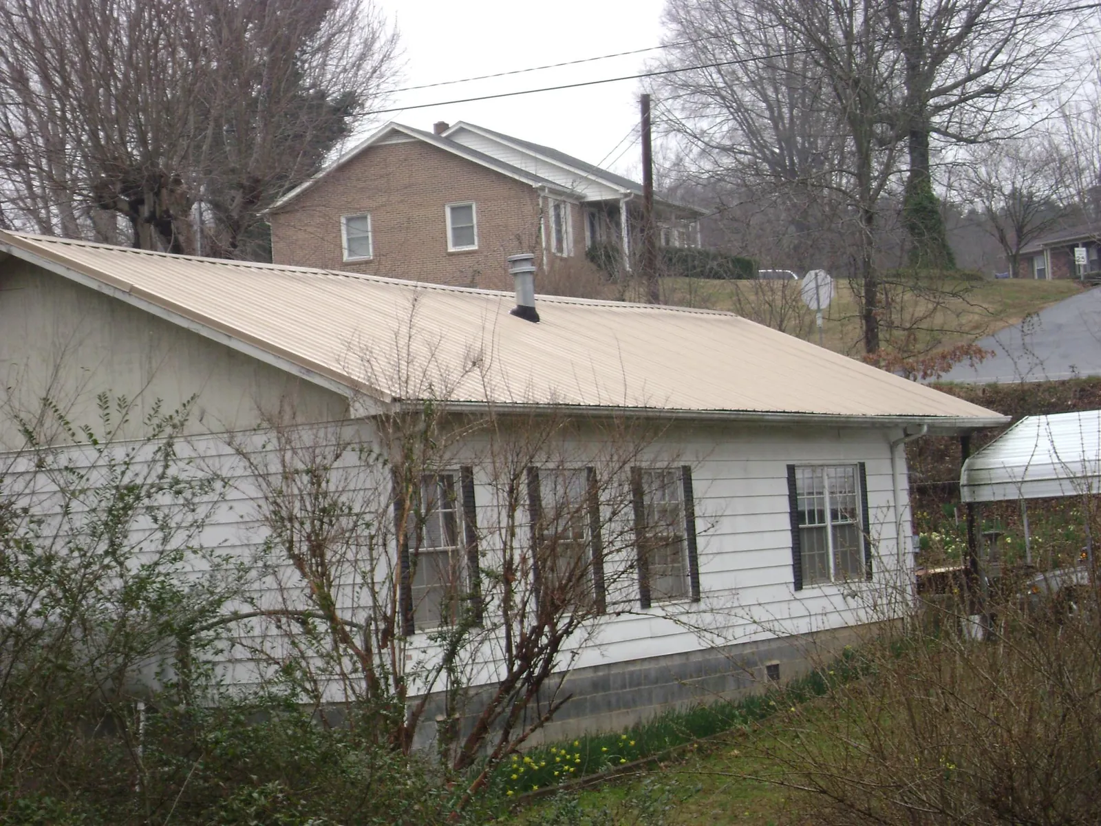 Tan metal roof on a white sided house set into a hillside — Commercial Roofing by Roofing Brothers in Exira